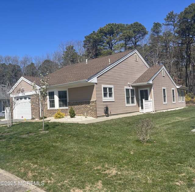 ranch-style home featuring a front lawn, roof with shingles, a garage, and brick siding
