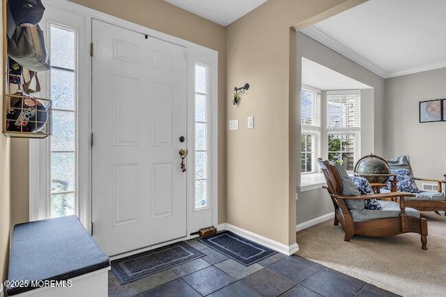 foyer entrance featuring baseboards, ornamental molding, stone finish floor, and a wealth of natural light