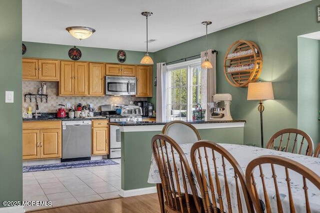 kitchen with backsplash, decorative light fixtures, dark countertops, appliances with stainless steel finishes, and a sink