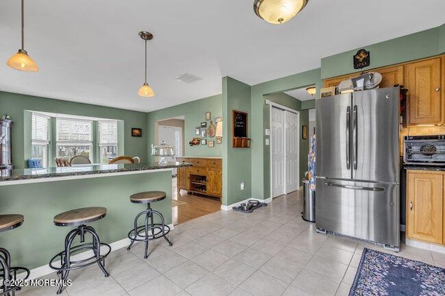 kitchen with hanging light fixtures, freestanding refrigerator, baseboards, light tile patterned floors, and a kitchen bar