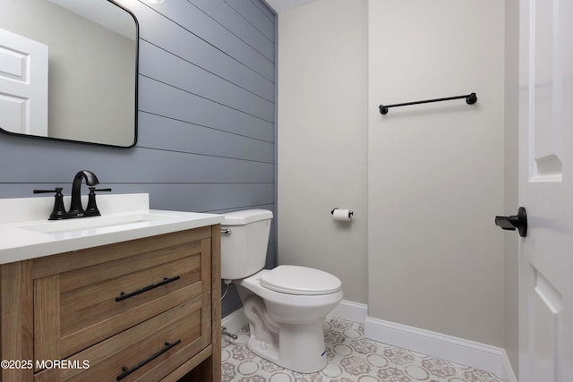 bathroom featuring baseboards, toilet, vanity, and wood walls