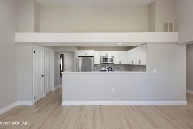 kitchen with light wood-type flooring, a towering ceiling, visible vents, backsplash, and appliances with stainless steel finishes