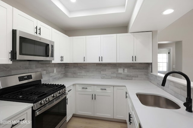 kitchen featuring recessed lighting, stainless steel appliances, backsplash, a sink, and white cabinetry