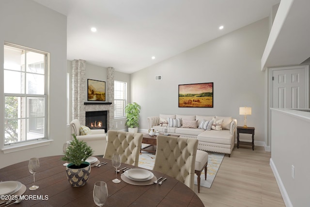living room featuring light wood-type flooring, vaulted ceiling, baseboards, visible vents, and a fireplace