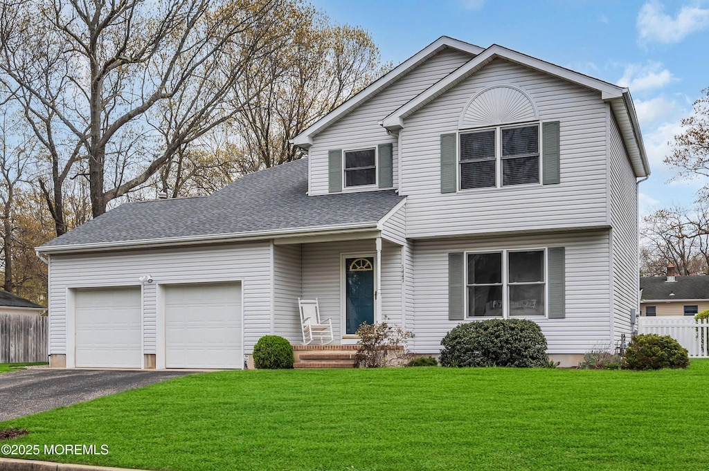 view of front facade with roof with shingles, driveway, fence, an attached garage, and a front yard