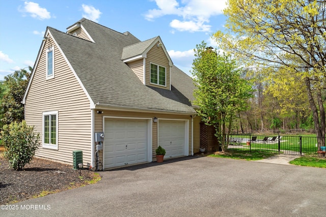 view of side of home with fence, aphalt driveway, roof with shingles, and a garage