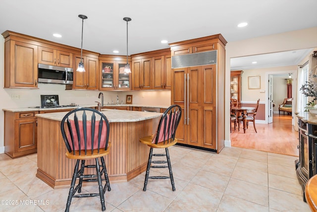 kitchen featuring built in fridge, brown cabinets, stainless steel microwave, and a center island with sink