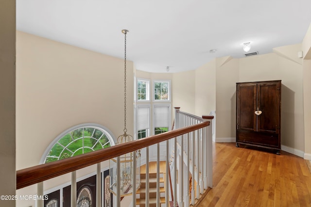 hall with baseboards, light wood-style flooring, visible vents, and an upstairs landing