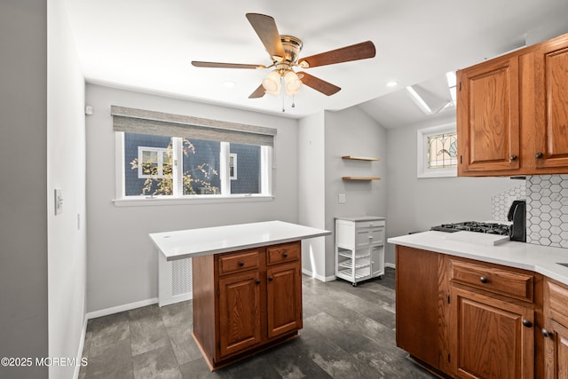 kitchen featuring brown cabinetry, baseboards, ceiling fan, light countertops, and backsplash