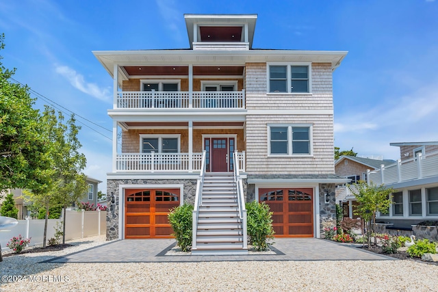 beach home featuring stone siding, covered porch, a garage, a balcony, and stairway
