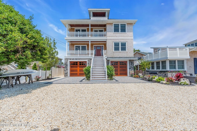 coastal inspired home featuring stairway, fence, a balcony, an attached garage, and stone siding