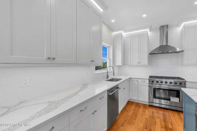 kitchen with wall chimney exhaust hood, stainless steel appliances, a sink, decorative backsplash, and light stone counters