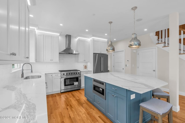 kitchen featuring white cabinets, wall chimney range hood, a sink, high quality appliances, and blue cabinetry