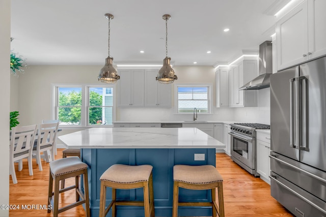kitchen featuring high end appliances, a kitchen breakfast bar, a sink, wall chimney exhaust hood, and a center island