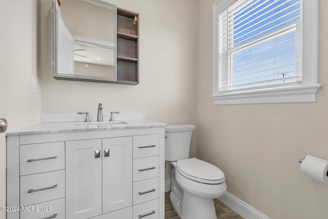 half bath with a healthy amount of sunlight, toilet, baseboards, and vanity