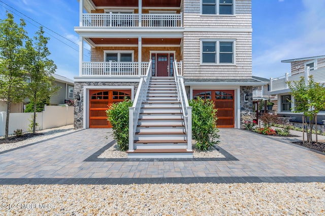 raised beach house with an attached garage, stone siding, stairs, and decorative driveway