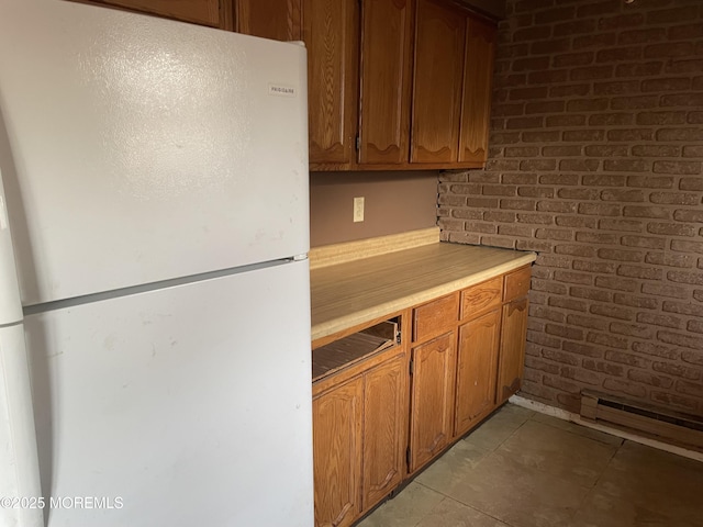 kitchen featuring light countertops, freestanding refrigerator, brown cabinets, and brick wall