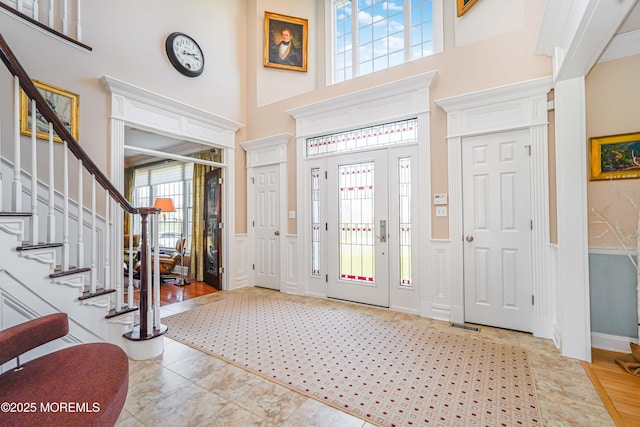 foyer entrance featuring visible vents, wainscoting, a high ceiling, and stairway