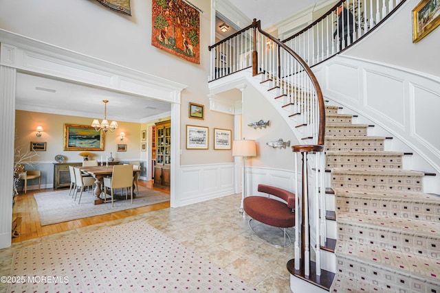 stairs with crown molding, wainscoting, a decorative wall, and a notable chandelier