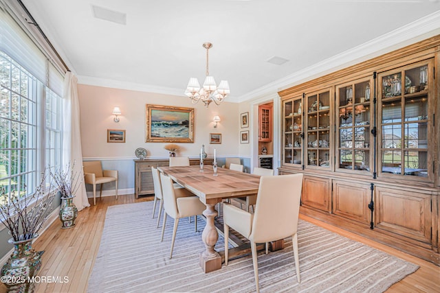 dining area with an inviting chandelier, a wainscoted wall, crown molding, and light wood-style floors