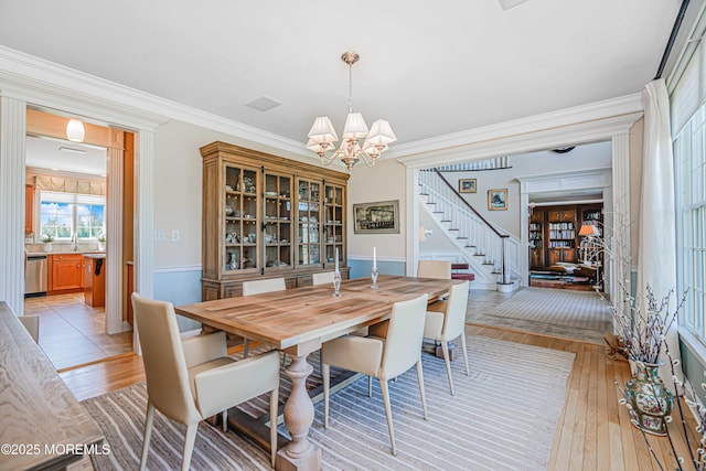 dining space featuring crown molding, a notable chandelier, light wood-style flooring, and stairway