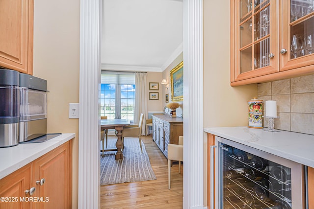 bar with light wood-style floors, beverage cooler, backsplash, ornamental molding, and a bar