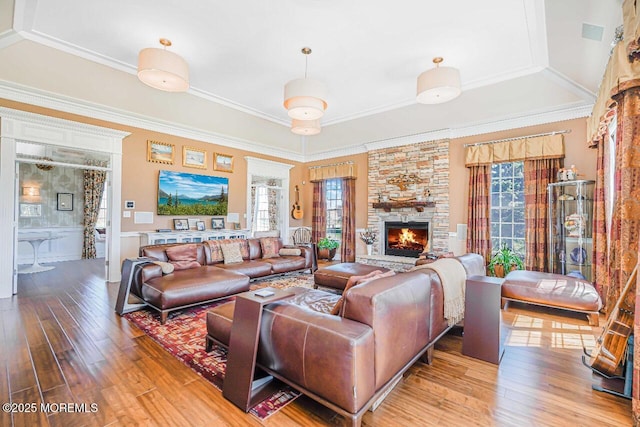 living room featuring a stone fireplace, wainscoting, wood finished floors, and a healthy amount of sunlight