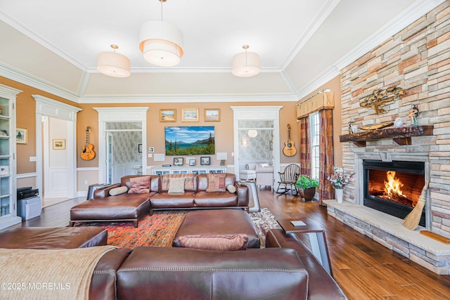 living room with a stone fireplace, ornamental molding, wainscoting, and wood finished floors