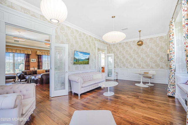 living area with wallpapered walls, ornamental molding, wood finished floors, and a wainscoted wall