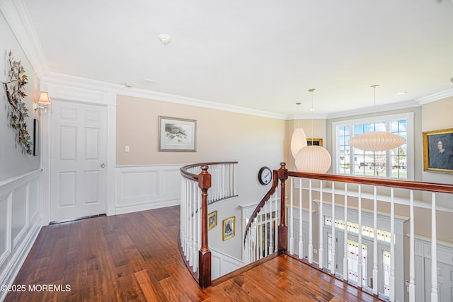 hallway featuring crown molding, wainscoting, a decorative wall, wood finished floors, and an upstairs landing