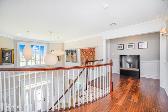 corridor featuring a wainscoted wall, an upstairs landing, wood finished floors, visible vents, and ornamental molding