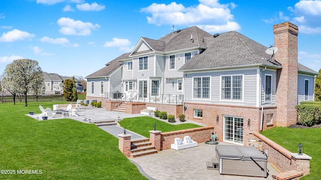 rear view of property featuring a chimney, a lawn, a hot tub, a patio, and a fire pit
