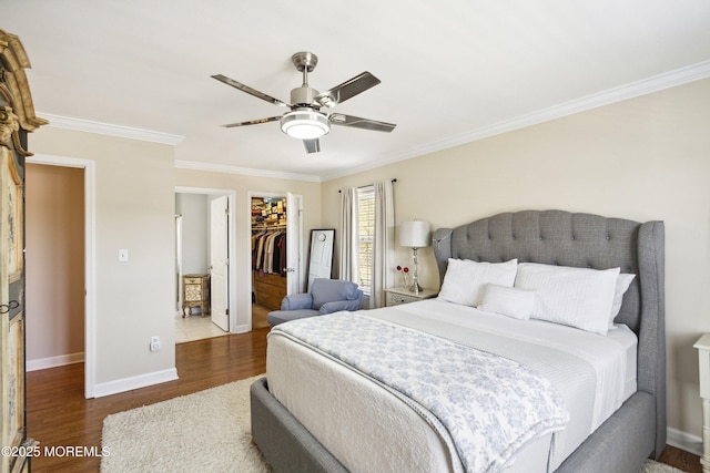 bedroom featuring a walk in closet, wood finished floors, baseboards, a closet, and ornamental molding