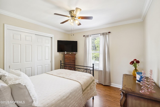 bedroom with ceiling fan, crown molding, wood finished floors, baseboards, and a closet