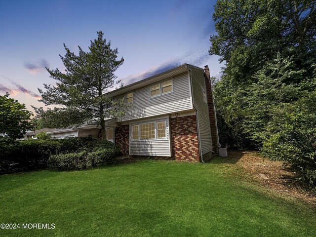 11 Green Hills Rd, East Brunswick, NJ 08816 - back of house at dusk featuring brick siding, a lawn, and a chimney