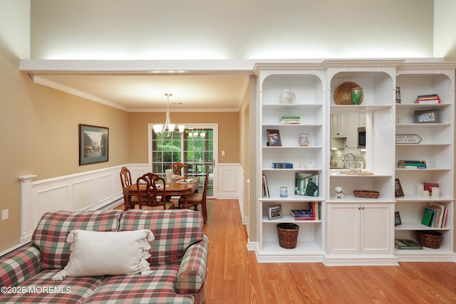 sitting room with crown molding, light wood-style floors, a decorative wall, and wainscoting