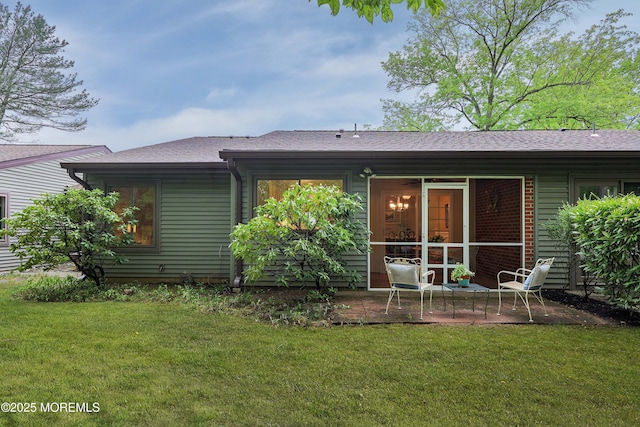 rear view of property with roof with shingles, a patio, and a lawn