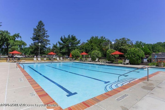 community pool featuring a patio area, fence, and view of wooded area