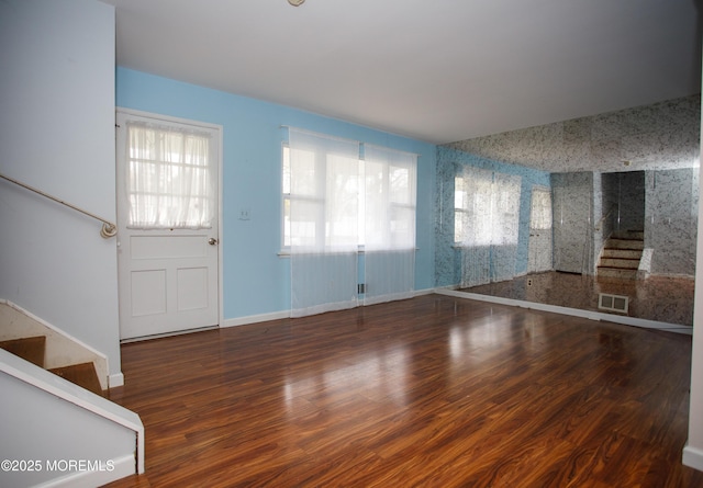 unfurnished living room with stairway, baseboards, wood finished floors, and visible vents