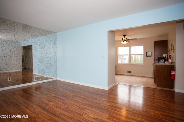 spare room with wood finished floors, visible vents, a ceiling fan, and baseboards