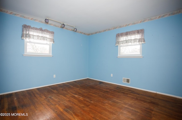 spare room featuring baseboards, a healthy amount of sunlight, hardwood / wood-style floors, and visible vents