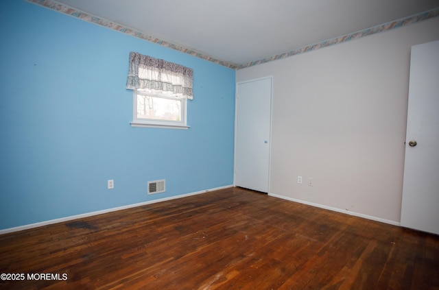unfurnished room featuring baseboards, visible vents, and wood-type flooring