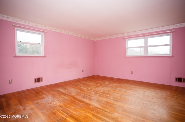 empty room with light wood finished floors, visible vents, and plenty of natural light