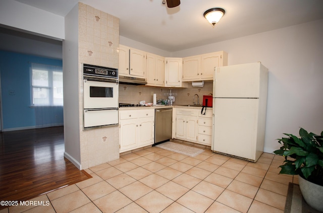 kitchen with under cabinet range hood, a sink, white appliances, a warming drawer, and decorative backsplash