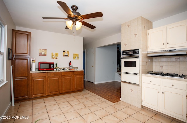 kitchen featuring oven, a warming drawer, decorative backsplash, ceiling fan, and gas stovetop