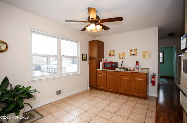 kitchen with brown cabinets, visible vents, baseboards, and ceiling fan