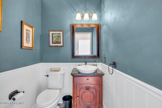 bathroom with a wainscoted wall, vanity, toilet, and a decorative wall