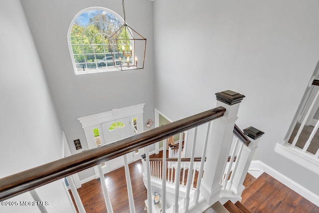 stairway featuring plenty of natural light, a towering ceiling, wood finished floors, and a notable chandelier