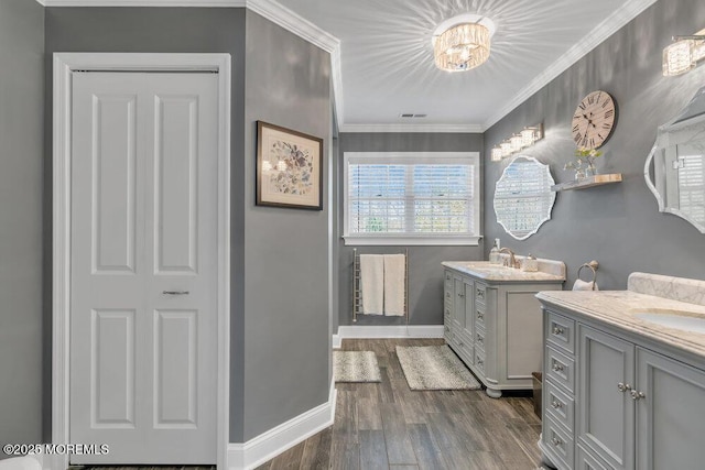 full bath with crown molding, baseboards, two vanities, and wood finished floors