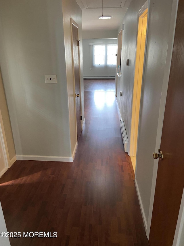 corridor with dark wood finished floors, baseboards, attic access, and a baseboard heating unit